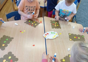 Dzieci przy stoliku ozdabiają sylwety pierniczków.